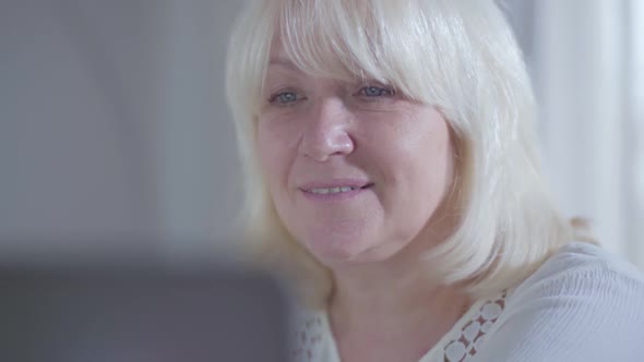 Close-up Face of Attractive Mature Caucasian Woman Looking at Laptop Screen and Smiling