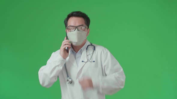 Asian Doctor With Stethoscope Wearing Mask, Talking On Mobile Phone While Running On Green Screen