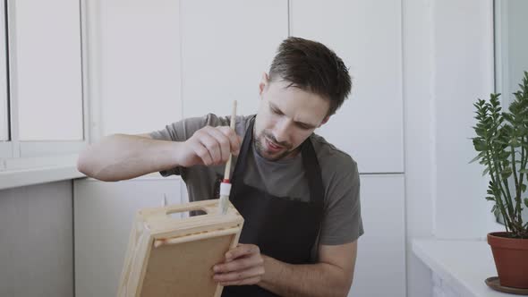 Young Craftman in Black Apron Paints Wooden Handmade Box with a White Liquid