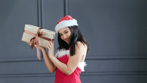 Sexy Beautiful Asian Young Woman Wearing Santa Claus Suit Smiling and Holding Gift Box at Studio