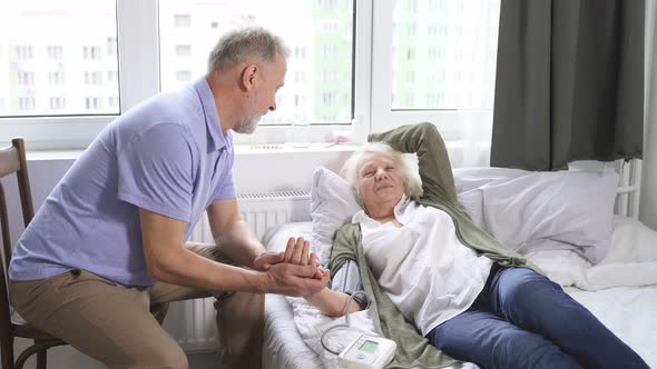 an Elderly Man Uses a Blood Pressure Monitor To Measure the Blood Pressure of His Beloved Wife Who