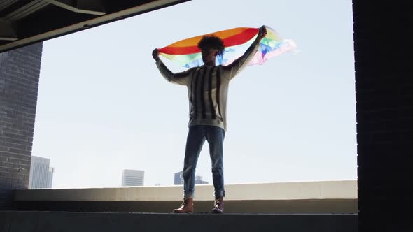 African american man holding lbgt flag while standing near the window