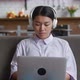 Asian Woman with Headphones Resting on Couch Using Laptop Computer Looking at Screen Typing Message - VideoHive Item for Sale