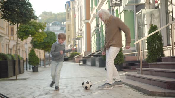 Wide Shot of Happy Grandfather and Grandson Playing Football Outdoors on City Street and Giving High