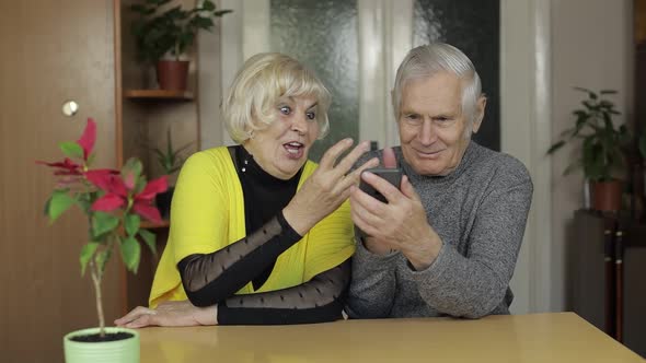 Pretty Mature Senior Couple Grandparents Enjoy Online Shopping on Phone at Home