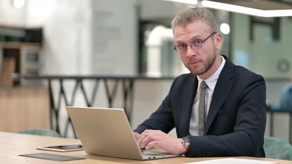 Businessman with Laptop Smiling at Camera in Office 