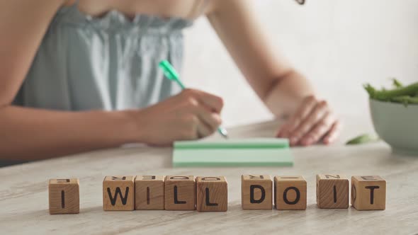 Motivational Message, Slogan I Will Do It Laid Out From Cubes. Young Woman Writes In Notebook