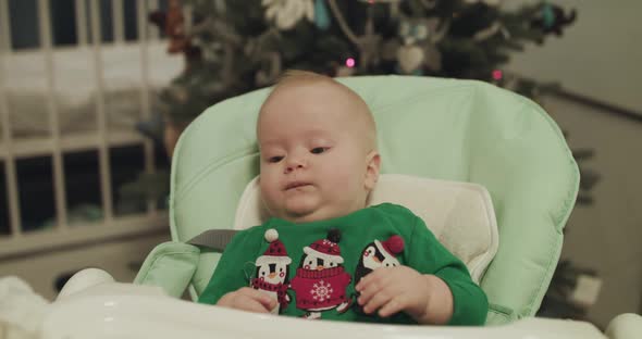 Beautiful Look of Christmas Toddler in Kid Chair During Feeding with Spoon