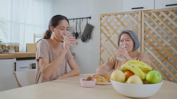 Asian young attractive daughter eating breakfast with senior mother.