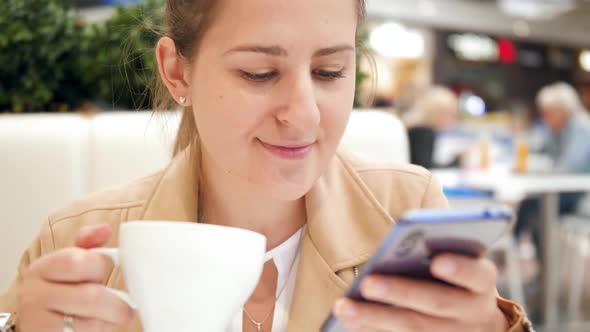 Closeup Video of Smiling Young Woman Browsing Internet on Smartphone and Drinking Coffee in Cafe at