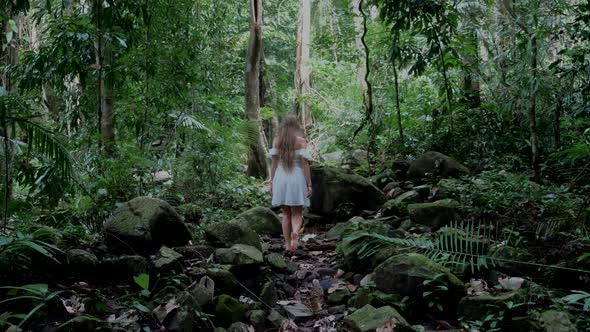 Back View of Beautiful Woman Walking Among Big Moss Stones in Tropical Jungle