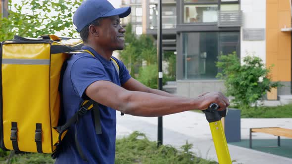Smiling Afroamerican Man Courier Delivery Walks Street with Electric Scooter