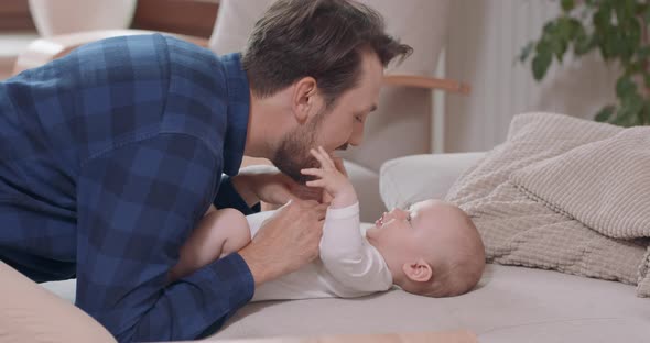Close of Bearded and Mustashed Father is Kneeling By the Baby Lying on the Couch Caresses Its Chest