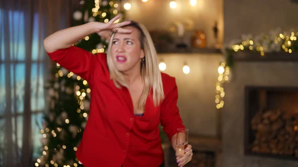 a Blonde in a Red Blazer Dances with a Glass Against the Background of a Christmas Tree and Lights