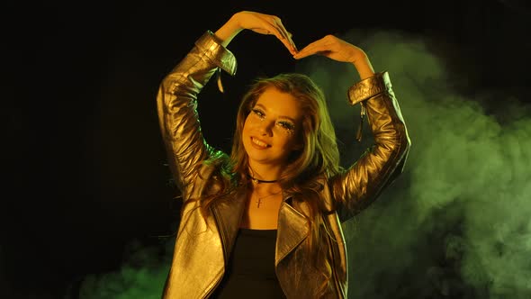 Portrait of Young Pretty Woman Is Looking at the Camera Shows a Heart Gesture with Her Hands. Close