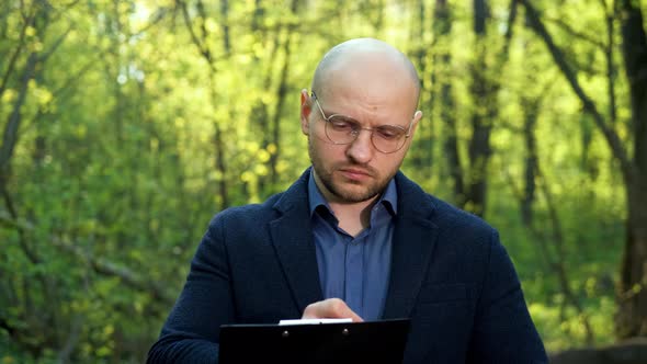 A Bald Intelligent Ecologist Man with a Beard and Glasses Writes Down Data