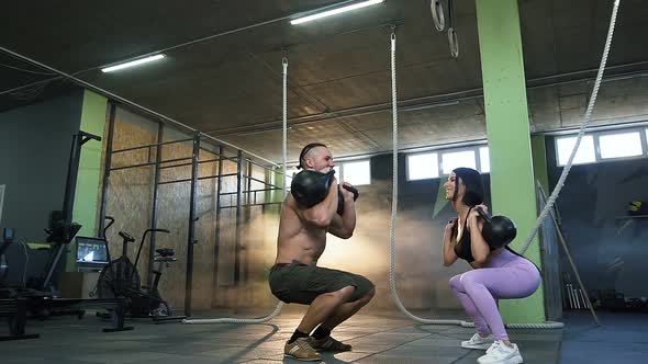 Attractive Fit Couple Squatting with Kettlebells in the Hands in Crossfit Gym