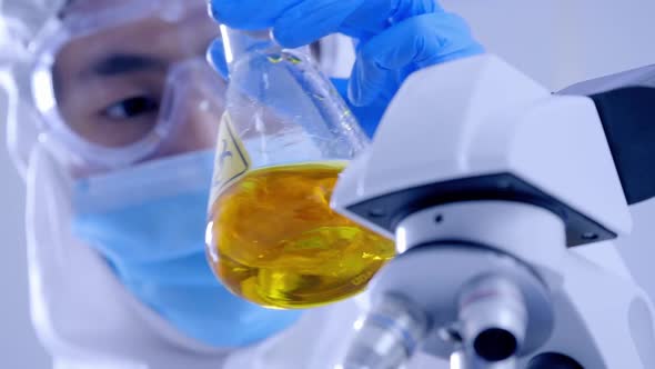 Scientist in PPE suite doing some research checking a liquid in a test tube at laboratory.