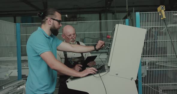 Two Engineers Work Behind the Control Panel of the Production Machine on Factory