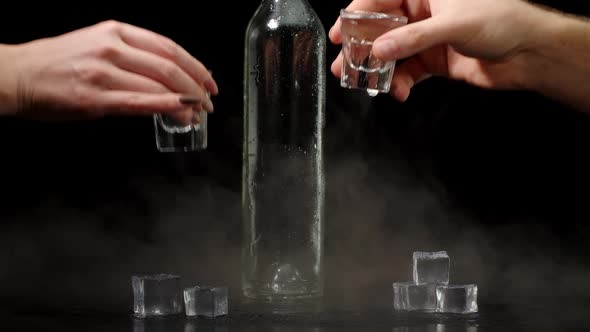 Two Hands with Glasses of Vodka Making Cheers Raising Toast on Black Background with Ice Cubes