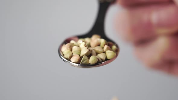 Close up green buckwheat is pouring from a metal spoon