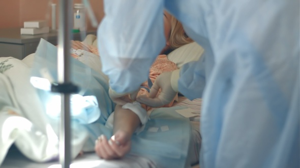 Nurse in gloves and mask putting female patient on a drip