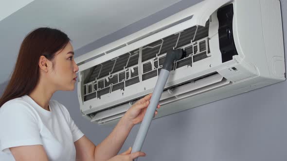 young woman using vacuum cleaner to cleaning the air conditioner at home