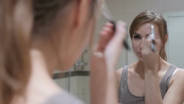 Young Woman Putting Makeup on Face in Mirror