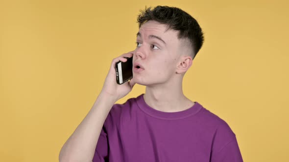 Young Man Talking on Smartphone on Yellow Background