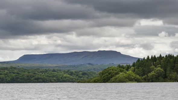 Time lapse of lake with forest and hill in the distance on a cloudy day in Ireland. alt