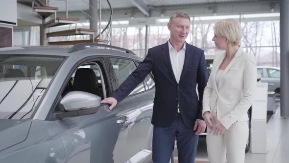 Confident Caucasian Businesswoman Choosing Car in Dealership. Smiling Dealer Consulting Client in