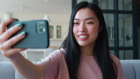 Closeup of Young Asian Woman Holding Smart Phone in Outstretched Arm Looking at Web Camera Smiling