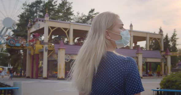 Back View of Young Woman in Safety Mask at Empty Amusement Park