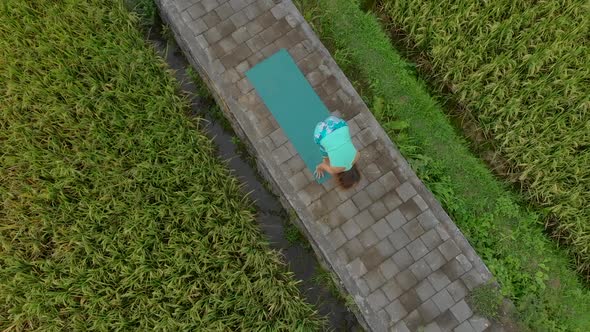 Aerial Slowmotion Shot of a Young Woman Practicing Yoga on a Beautiful Rice Field