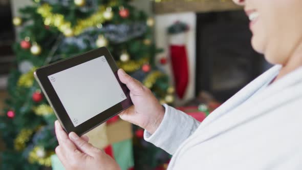 Happy mixed race senior woman on video call on tables with copy space at christmas time