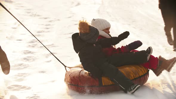 A Man Father Rolls His Kids on the Inflatable Sled Around Himself