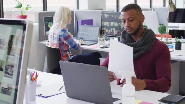 Mixed race businessman using laptop going through paperwork in modern office