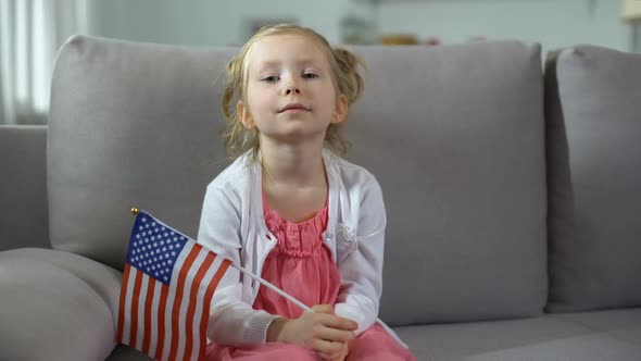 Little Proud Girl Holding Flag of USA, Resting on Sofa at Home, Independence Day