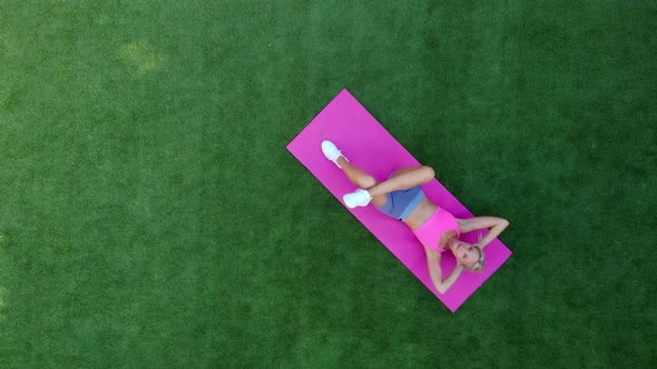 Top View Young Sporty Woman Performs Twisting While Lying on Grass