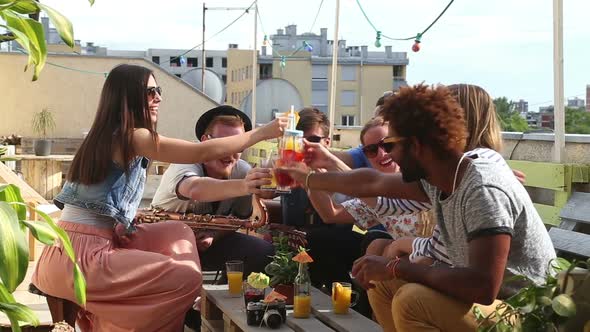 Cheerful multi-ethnic friends laughing and toasting with cocktails at rooftop