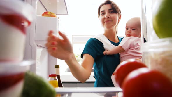 Mother with Baby Taking Food From Fridge at Home