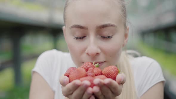 Close-up of Beautiful Woman Smelling Tasty Organic Strawberries and Smiling at Camera. Portrait of