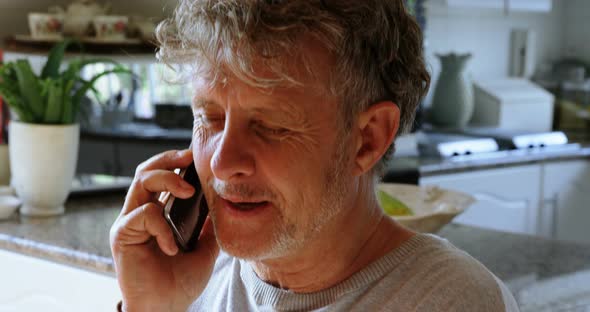 Senior man talking on mobile phone in kitchen at home