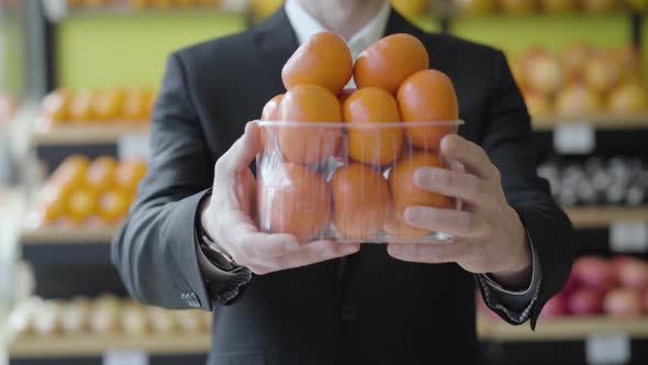 Unrecognizable Caucasian Man in Suit Stretching Basket of Delicious Juicy Tangerines To Camera. Male