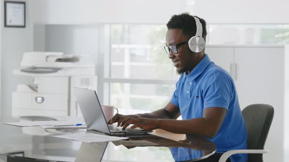 Cheerful African Manager Listening to Music in Headphones Working on Laptop