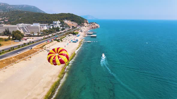 The red-yellow parachute is shading behind the boat. Parasailing in Turkey. Beautiful sandy beach an