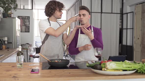 Young Gay Couple Cooking and Tasting Delicious Healthy Food Cooking in the Kitchen