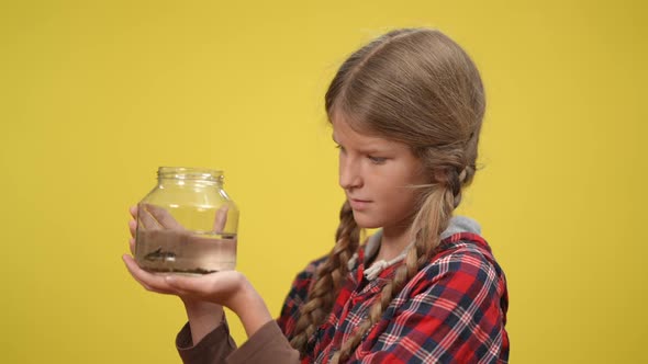 Side View Slim Teenage Girl Holding Bottle with Fish Standing at Yellow Background