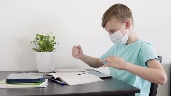 A Young Boy in a Face Mask Checks His Homework for School and Celebrates at a Table at Home