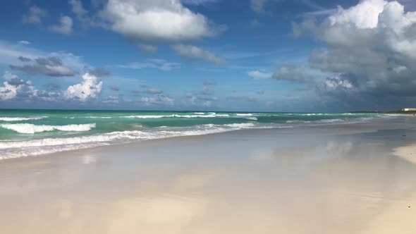 Slow motion camera pan along caribbean white sandy beach with cloud formations